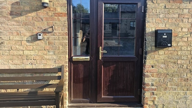 A dark wooden door with a glass panel, a bench, and a mailbox on a brick wall.