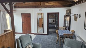 A cozy room with a wooden ceiling, a dining table with chairs, a sofa, and a mirror.