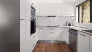 A modern kitchen with white cabinets, a built-in oven, a dishwasher, and a window with a view of trees.