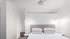 A modern hotel room with a large bed, two bedside tables, a round mirror, and a ceiling fan.