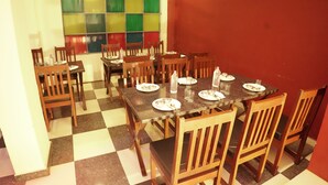 A dining area with a checkered floor, wooden chairs, and a table set for a meal. - Hotel Golden Bird (Pushkar)