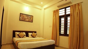 A neatly made bed with a headboard, a painting on the wall, and a window with curtains. - Hotel Golden Bird (Pushkar)