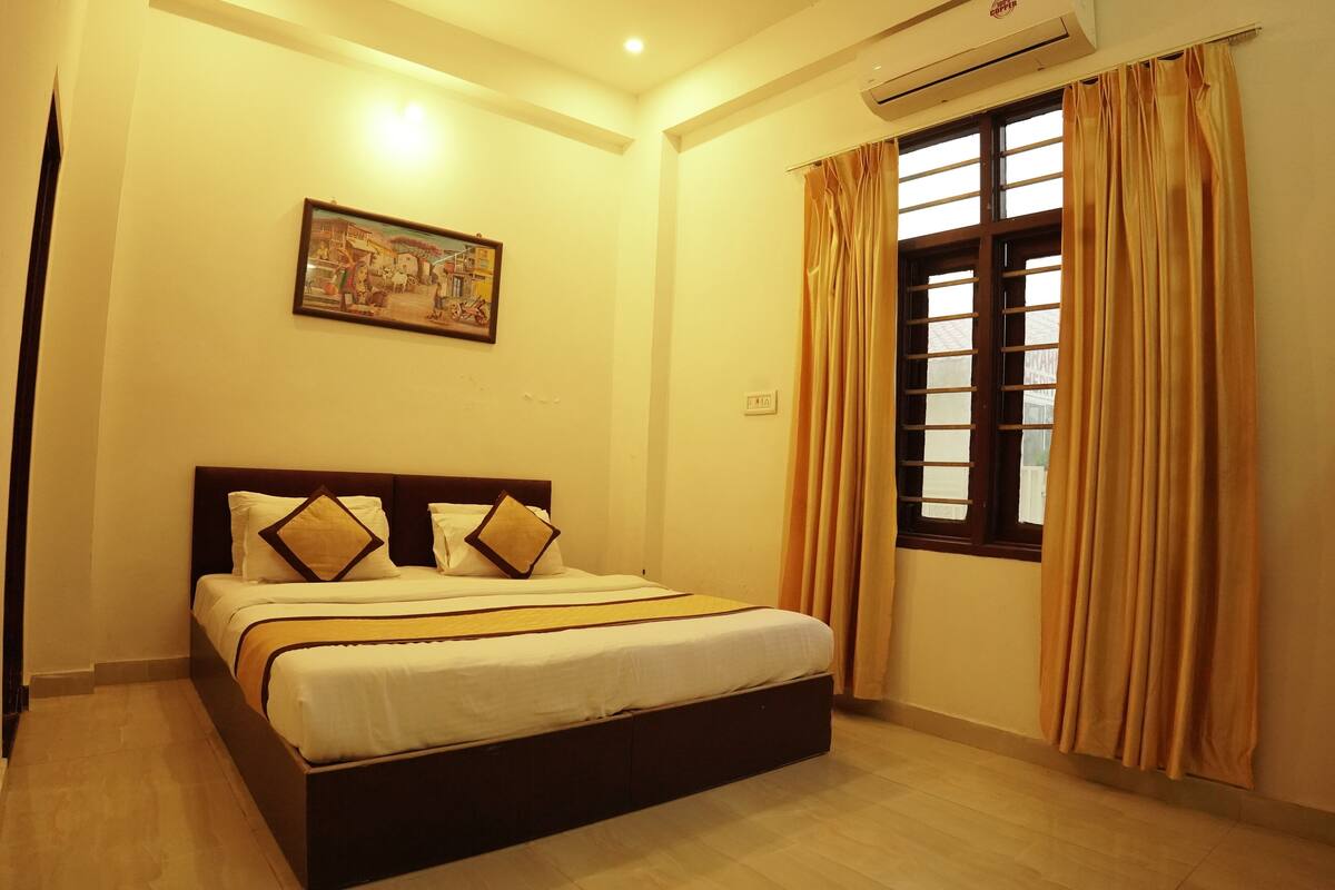 A neatly made bed with a headboard, a painting on the wall, and a window with curtains.
