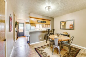 A modern kitchen with a central island, a dining area with a round table and chairs, and a hallway leading to a door.
