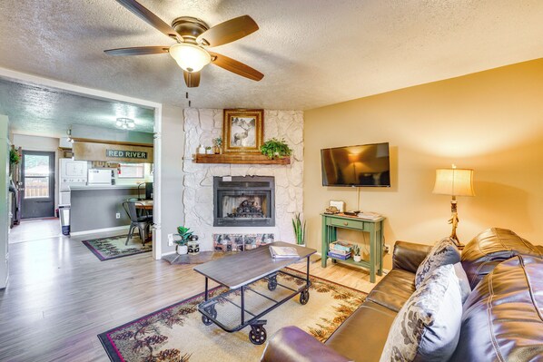 A living room with a fireplace, a ceiling fan, a television, and a sofa. - Hike, Bike & Ski: Red River Condo w/ Spa Access (Red River)