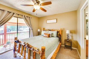 A bedroom with a wooden bed frame, a ceiling fan, a window with curtains, and a bedside table with a lamp. - Hike, Bike & Ski: Red River Condo w/ Spa Access (Red River)