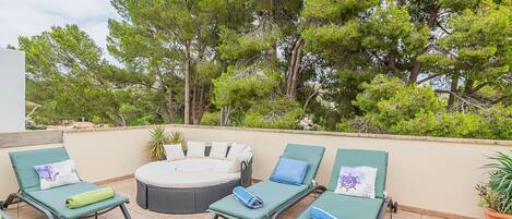 Una terraza en la azotea con cuatro sillones, una mesa redonda y una planta en maceta.