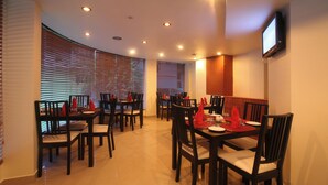 A dining area with multiple tables and chairs, equipped with ceiling lights and a flat-screen TV mounted on the wall.