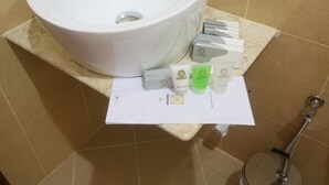 A bathroom with a white sink, a paper towel dispenser, and toiletries including a green bottle and a white bottle.