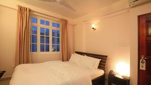 A neatly made bed in a room with a window, a bedside table with a lamp, and a door with a sign.
