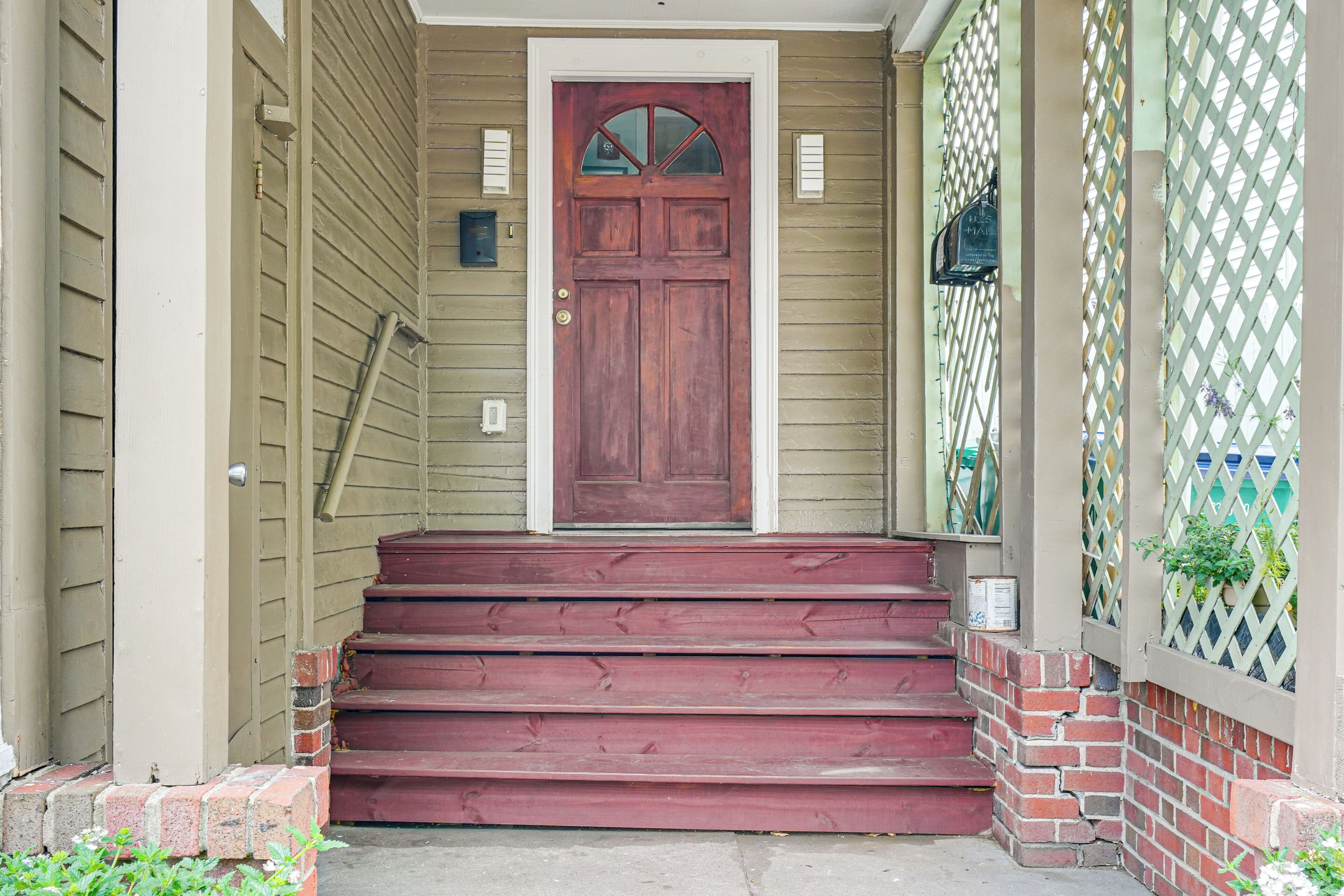 A wooden front door with a glass panel, a set of red steps leading up to it, and a lattice fence to the right.