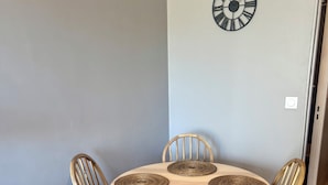 A dining area with a round table, six wooden chairs, and a wall-mounted clock.