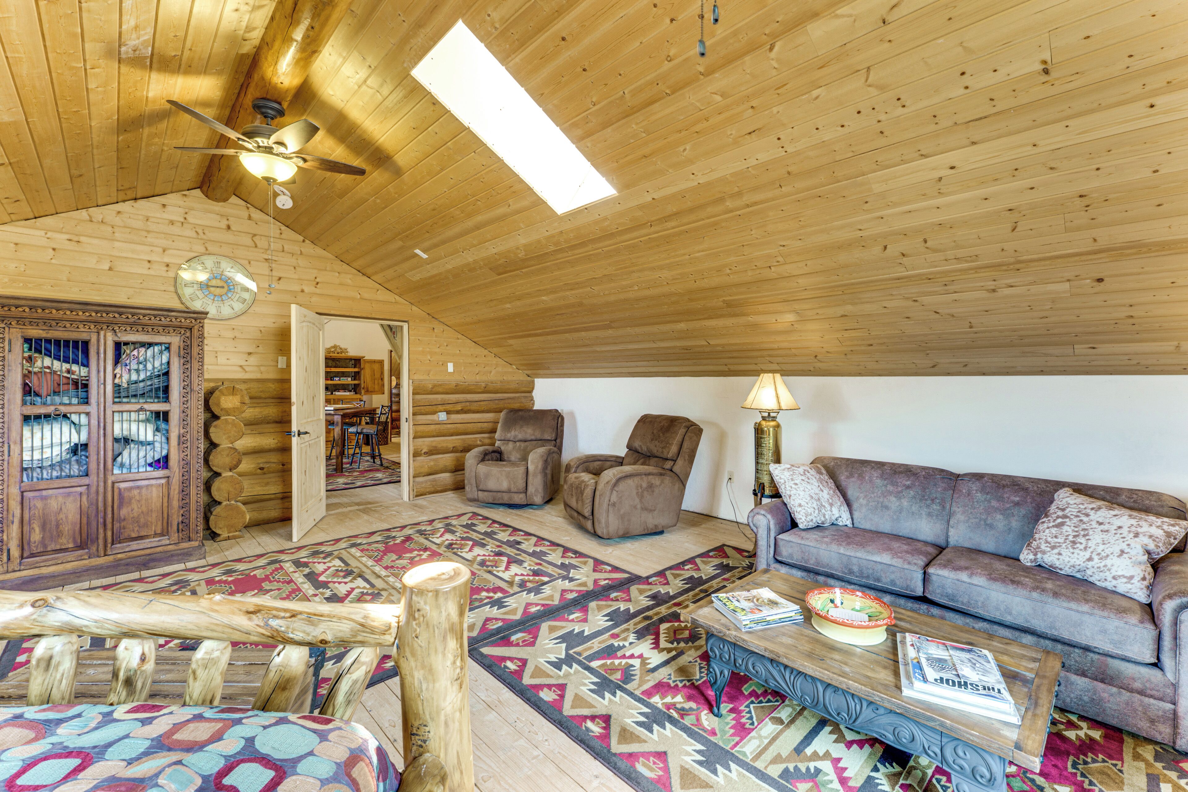 Interior d'una cabana de fusta amb sostre de fusta, un ventilador de sostre, un sofà, una taula de cafè i una catifes amb dibuixos.