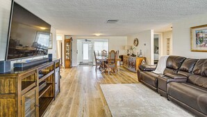 Een woonkamer met een flatscreen televisie, een houten tv-meubel, een leren bank, een eettafel en stoelen.