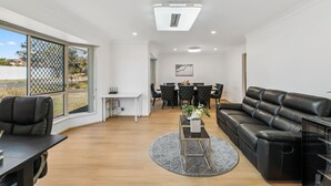 A spacious living area with a black leather sofa, a dining table with chairs, a white desk, and a large window with a view of the outdoors. - Spacious Family Retreat in Peaceful Parkinson (Parkinson)