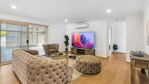 A living room with a sectional sofa, a round coffee table, a TV, and a small dining table. - Spacious Family Retreat in Peaceful Parkinson (Parkinson)