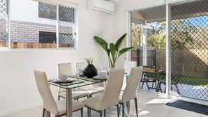 A dining area with a glass table, white chairs, and a potted plant.