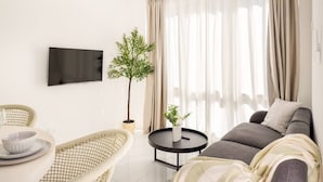 Ein modernes Wohnzimmer mit einer Couch, einem runden Couchtisch, Korbstühlen, einem Flachbildfernseher und einer Zimmerpflanze.