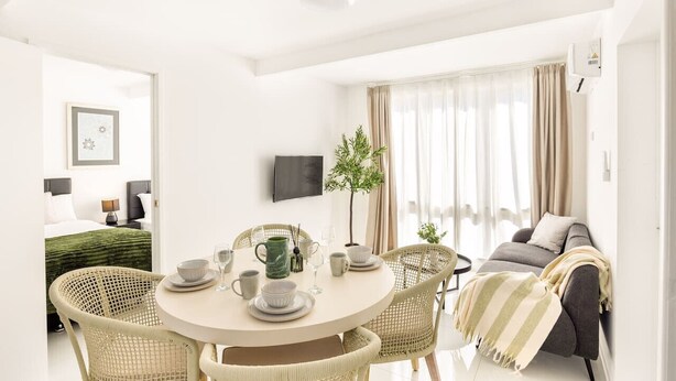 Ein modernes Hotelzimmer mit Essbereich, einer Couch und einem an der Wand befestigten Fernseher.