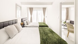 Ein modernes Hotelzimmer mit zwei Betten, einer grünen Tagesdecke und Blick auf den angrenzenden Wohnbereich.