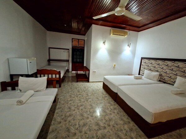 Habitación de hotel con dos camas, un escritorio, una silla, un ventilador de techo y un equipo de aire acondicionado.