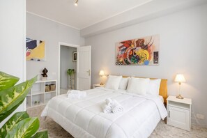 Een hotelkamer met een groot bed, twee bedlampen, een schilderij aan de muur en een klein plantje op een plank.