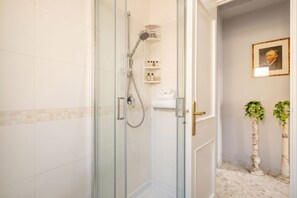 Een glazen douchecabine met een handdouche, een handdoekhouder en een plank met toiletartikelen.