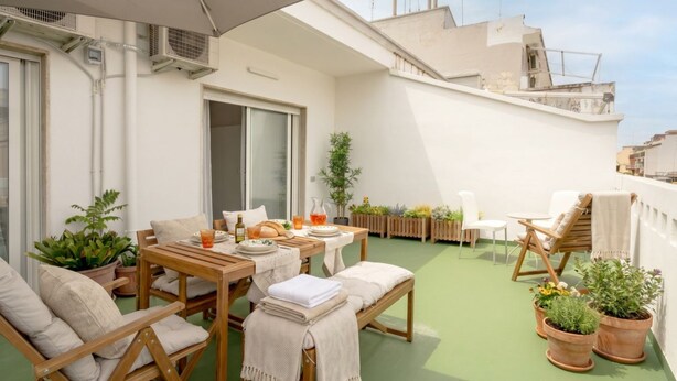 Une terrasse sur le toit, avec une table à manger, des chaises, des plantes en pot et une vue sur le paysage urbain.