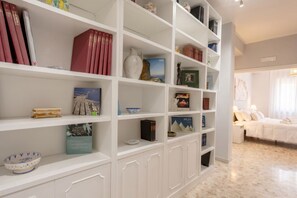 A white bookshelf with books, decorative items, and a bed in the background.