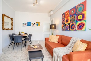 Een moderne woonkamer met een eethoek, een bank, een salontafel en een kleurrijk abstract schilderij aan de muur.