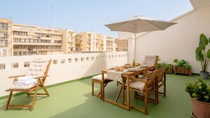Un balcon avec une table en bois, des chaises et un parasol.
