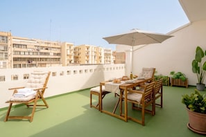 A balcony with a wooden table, chairs, and an umbrella. - The Rooftop – Modern Comfort with Outdoor Living (Bari)