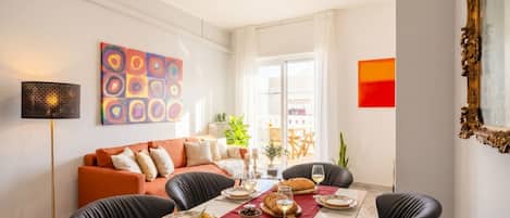 A dining area with a table set for four, a sofa, a lamp, and a painting on the wall.