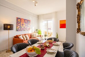 Een eethoek met een tafel gedekt voor vier personen, een bank, een lamp en een schilderij aan de muur.