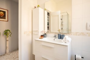 A bathroom with a white vanity, a mirror, a shower, and a potted plant. - The Rooftop – Modern Comfort with Outdoor Living (Bari)