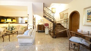 Un salon spacieux comprenant un canapé, des fauteuils, une table basse et un escalier agrémenté de rampes décoratives.