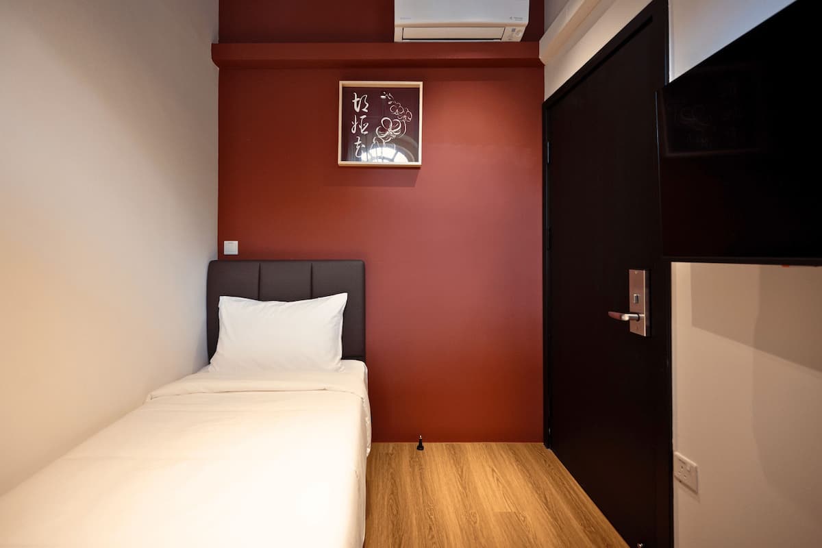 A hotel room with a bed, a wooden floor, a red accent wall, and a door.