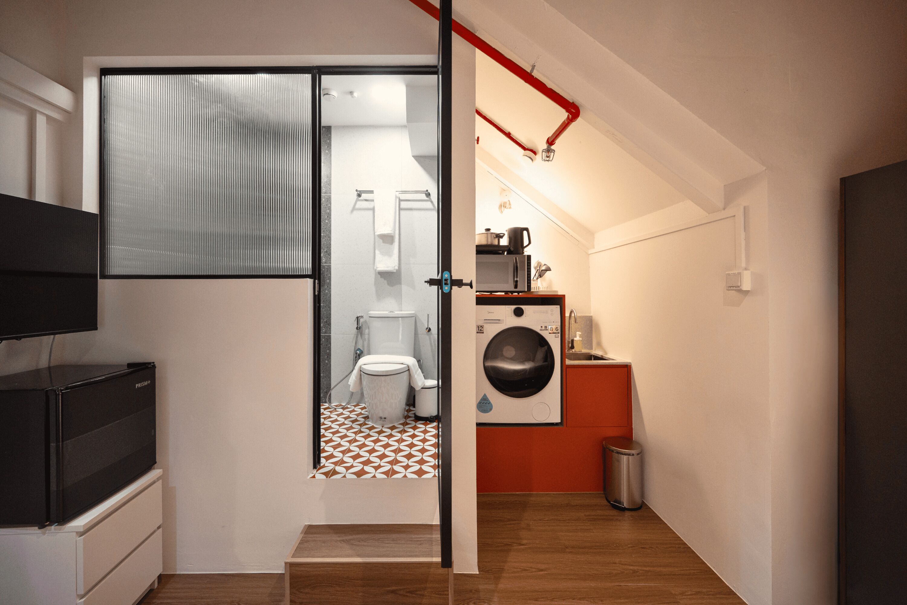 A compact living space with a kitchenette, a washing machine, and a television.