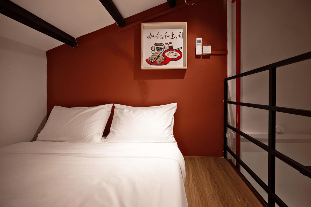 A bedroom with a bed, white bedding, a framed picture on the wall, and a wooden floor.