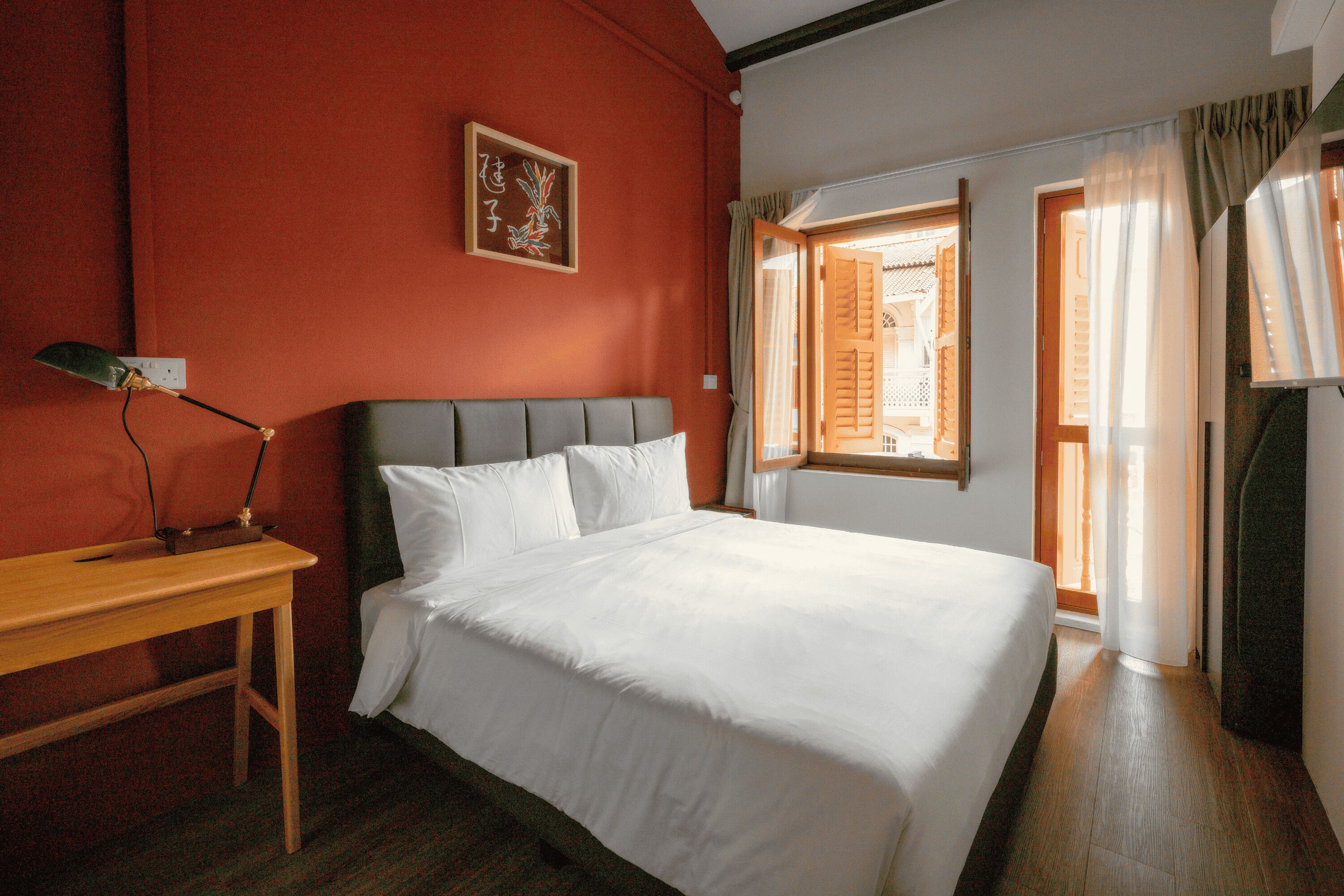 A hotel room with a bed, a desk, and a window with curtains.