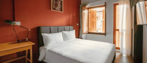 A hotel room with a bed, a desk, and a window with curtains.