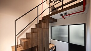 A modern staircase with wooden steps and metal railings, leading to a room with a large window and a black cabinet. - Hmlet Chinatown (Singapore)
