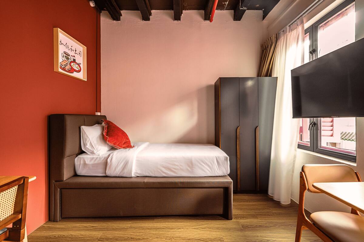 A compact bedroom with a bed, a wardrobe, a television, and a window with curtains.
