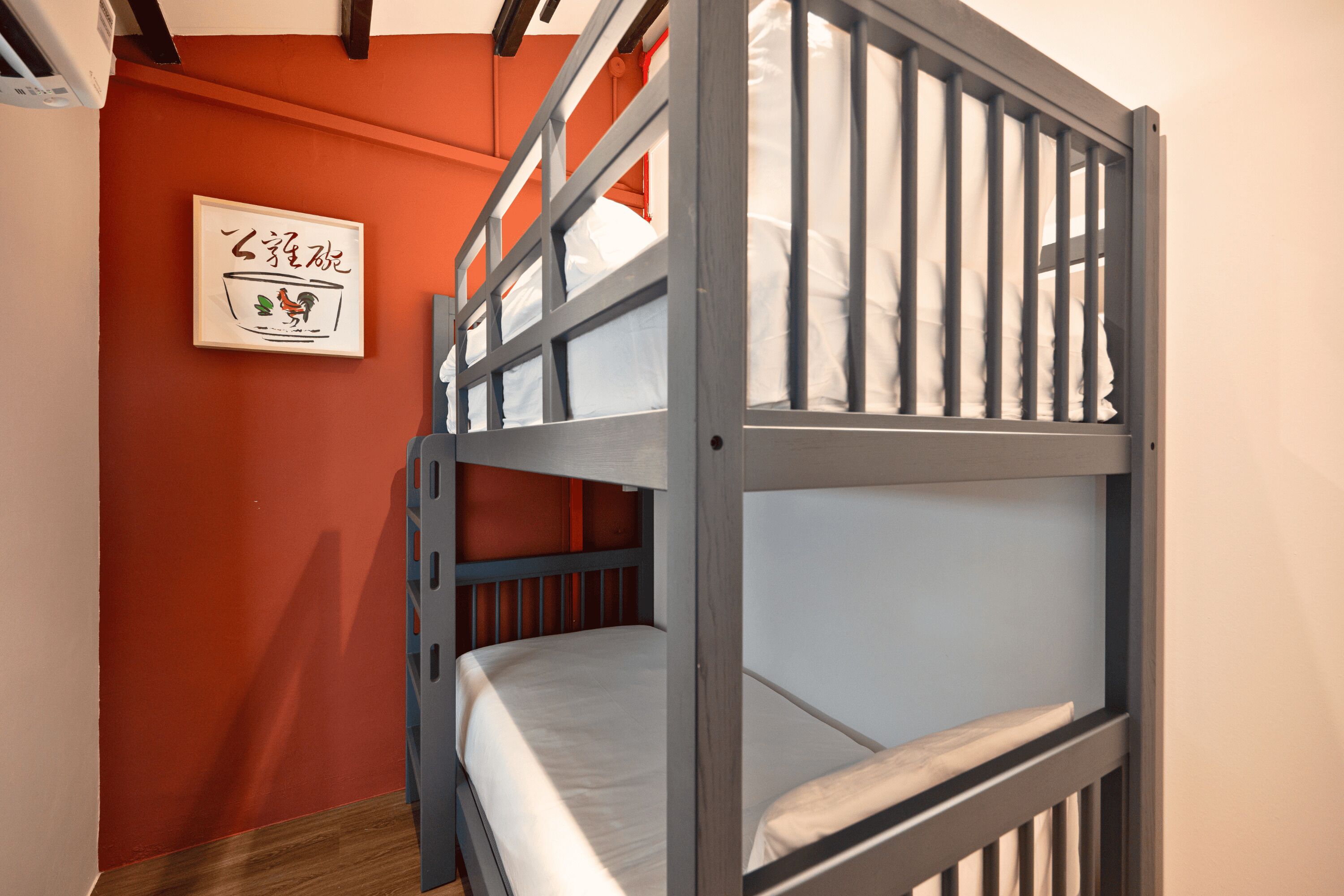 Ein Stockbett mit Kopfstütze an einer roten Wand, ein gerahmtes Bild und ein Holzboden.