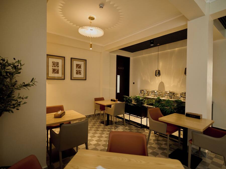 A dining area with checkered flooring, multiple tables and chairs, framed artwork on the walls, and a ceiling light fixture.