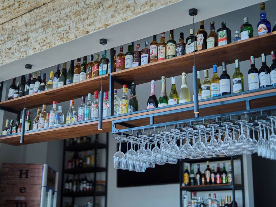Un espace bar avec des étagères remplies de bouteilles d’alcool et un présentoir à verres à vin.