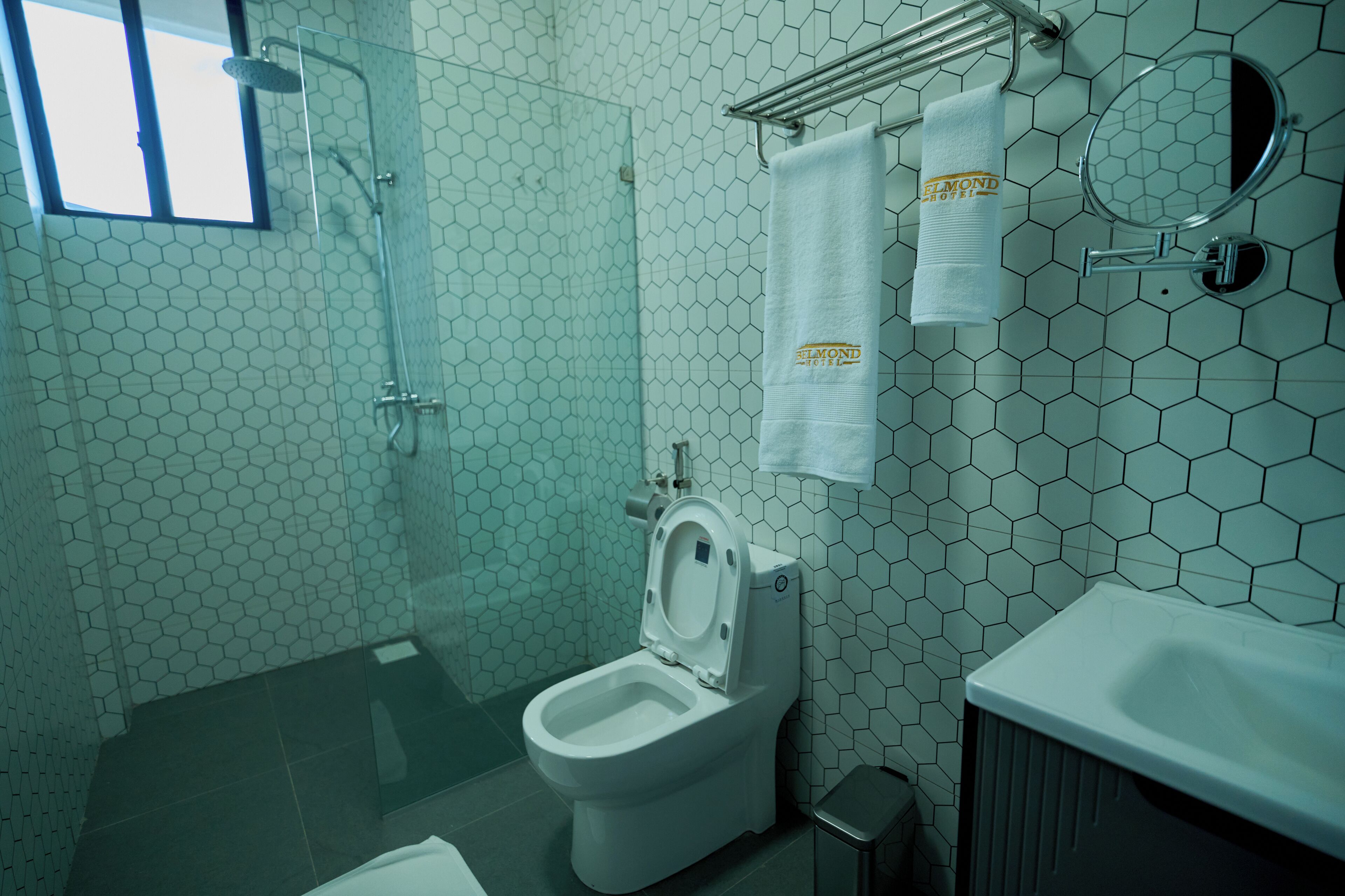 Un baño con un diseño de baldosas hexagonales, un inodoro, una ducha y un perchero con una toalla.