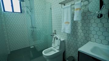 Un baño con un diseño de baldosas hexagonales, un inodoro, una ducha y un perchero con una toalla.