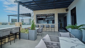 Zona de bar al aire libre con asientos y una barra llena de botellas.