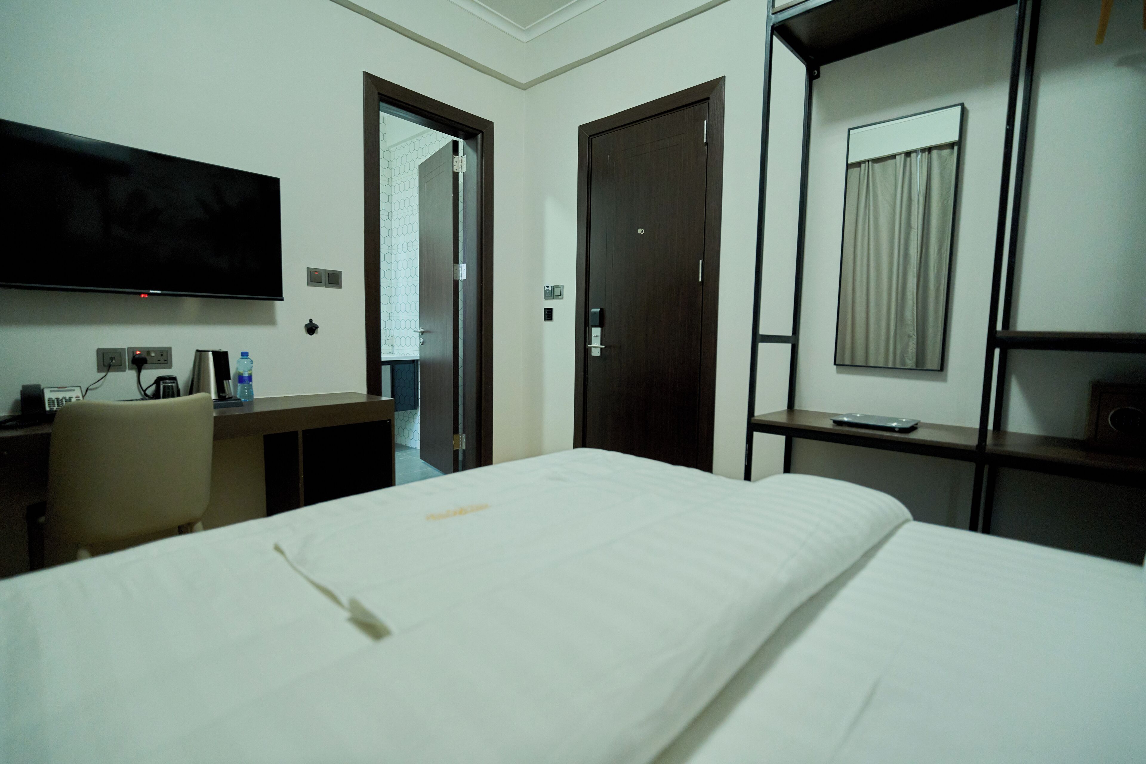 A hotel room with a bed, a desk with a chair, a flat-screen TV, and a wardrobe.
